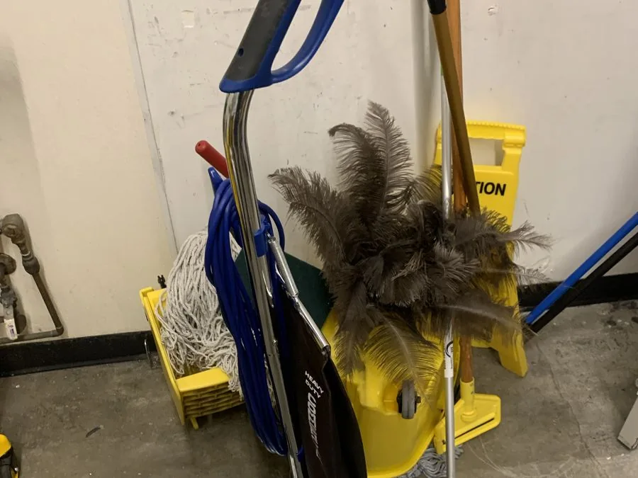 Mops, dusters, a floor-cleaning machine and yellow caution signs in a storage area