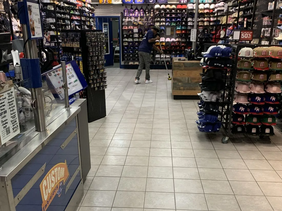 Cleaner working on a tiled aisle between hat displays in a retail store