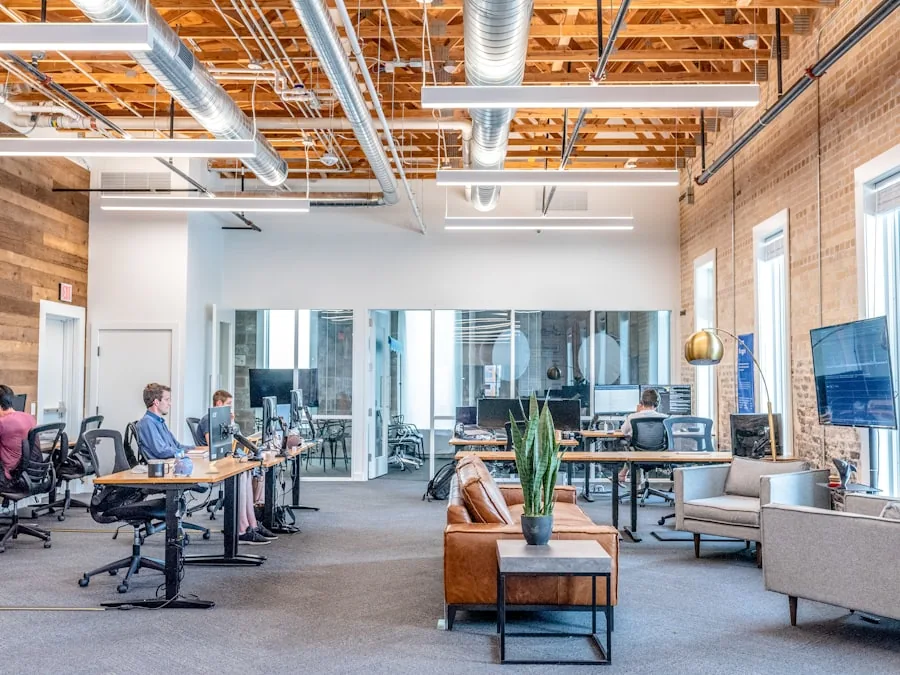 Open-plan office with desks, glass meeting rooms and a carpeted lounge area
