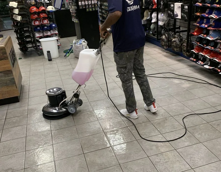 Cleaner guiding a rotary floor machine across wet tile in a hat store