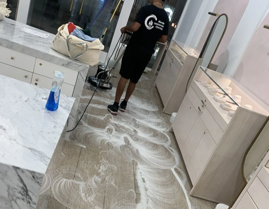 Cleaner operating a floor machine between glass display cases with cleaning solution on the floor