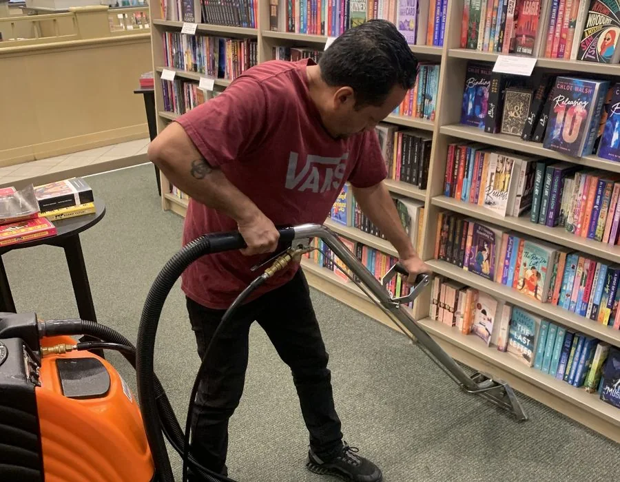 Cleaner using a carpet extraction wand beside bookshelves